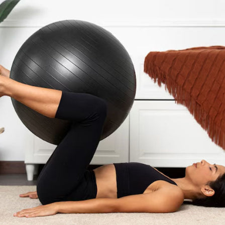Ballon pilates noir avec femme en position de pilates