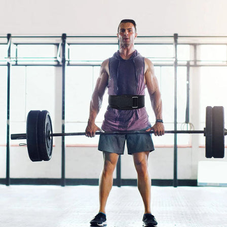 Un homme soulÚve une barre dans une salle de gym, équipé d'une ceinture de soutien pour le dos.