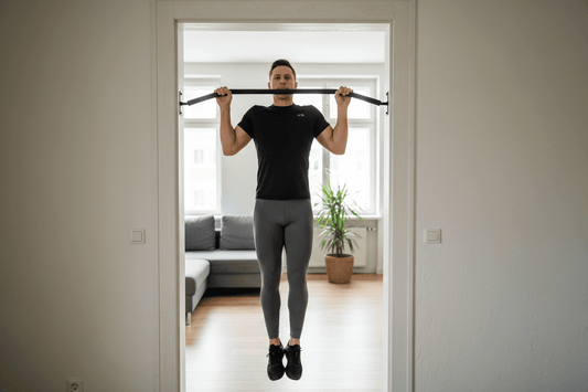 Homme réalisant une traction pull-up parfaite sur barre fixée dans l’embrasure d’une porte, barre devant le visage, pieds suspendus