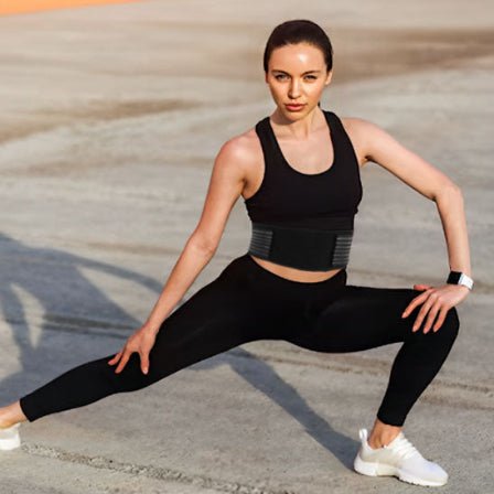 Une femme en tenue de sport noire s'étire, mettant en avant sa ceinture lombaire pour un soutien optimal.