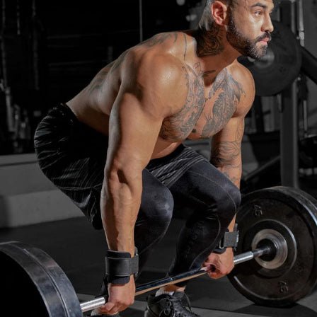 Un homme tient une barre de musculation avec des sangle de tirage, prêt à soulever un poids au sol.